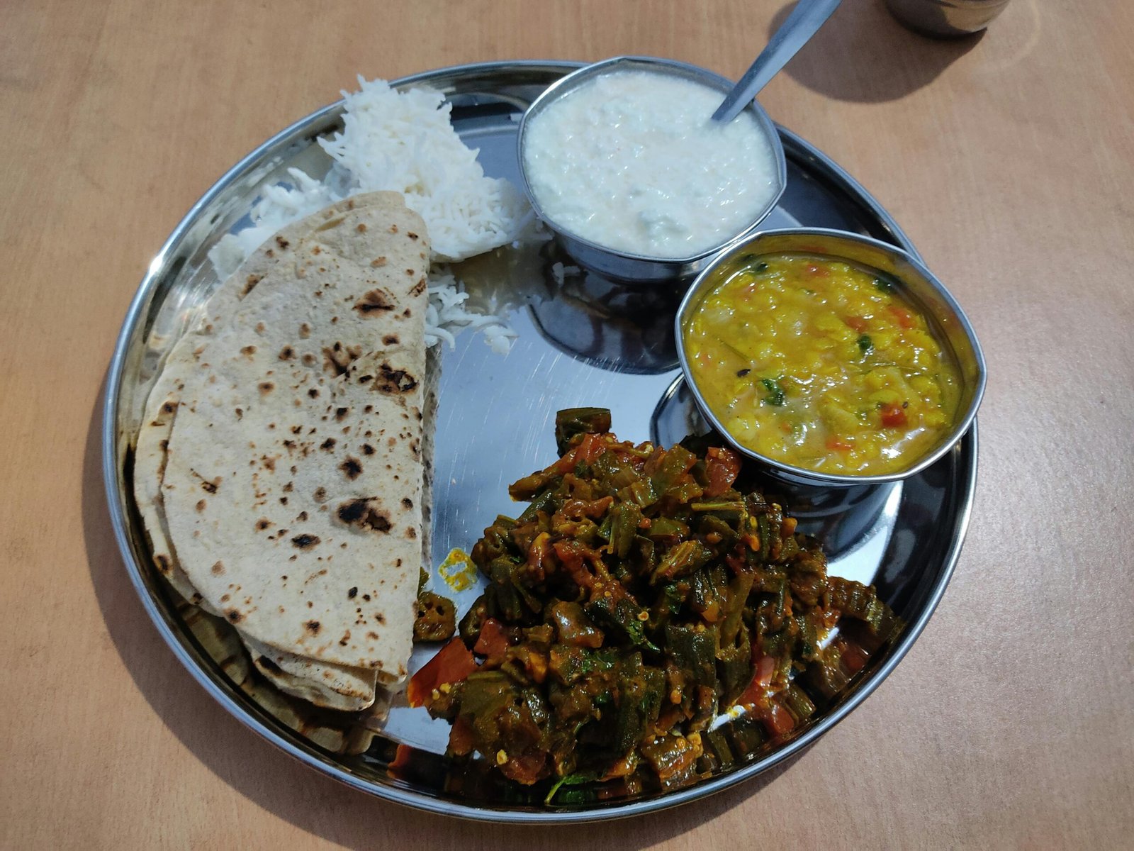 Indian steel thali with bhindi sabzi dal curd roti and rice showing authentic Indian vegetarian home meal