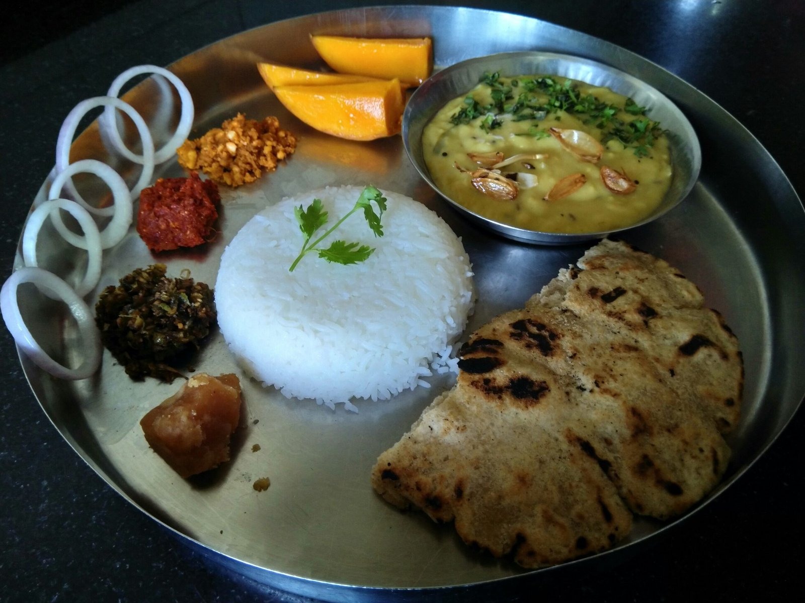 A complete North Indian vegetarian thali with roti, dal, sabzi, rice and raita on a steel plate