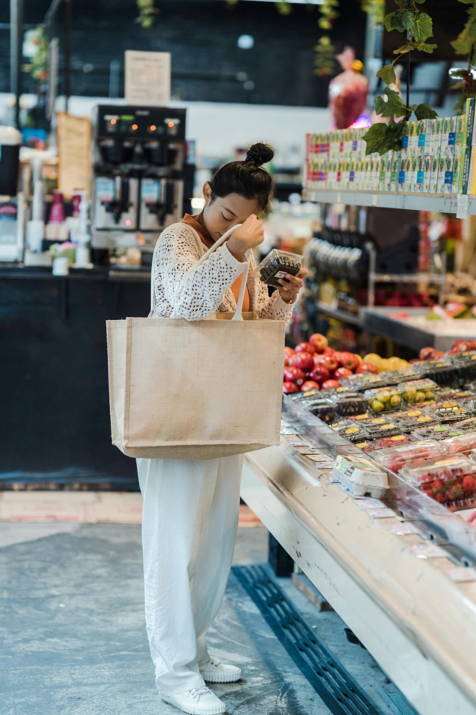 Woman grocery shopping with a tote bag checking labels at a fresh produce section for vegetarian meal plan